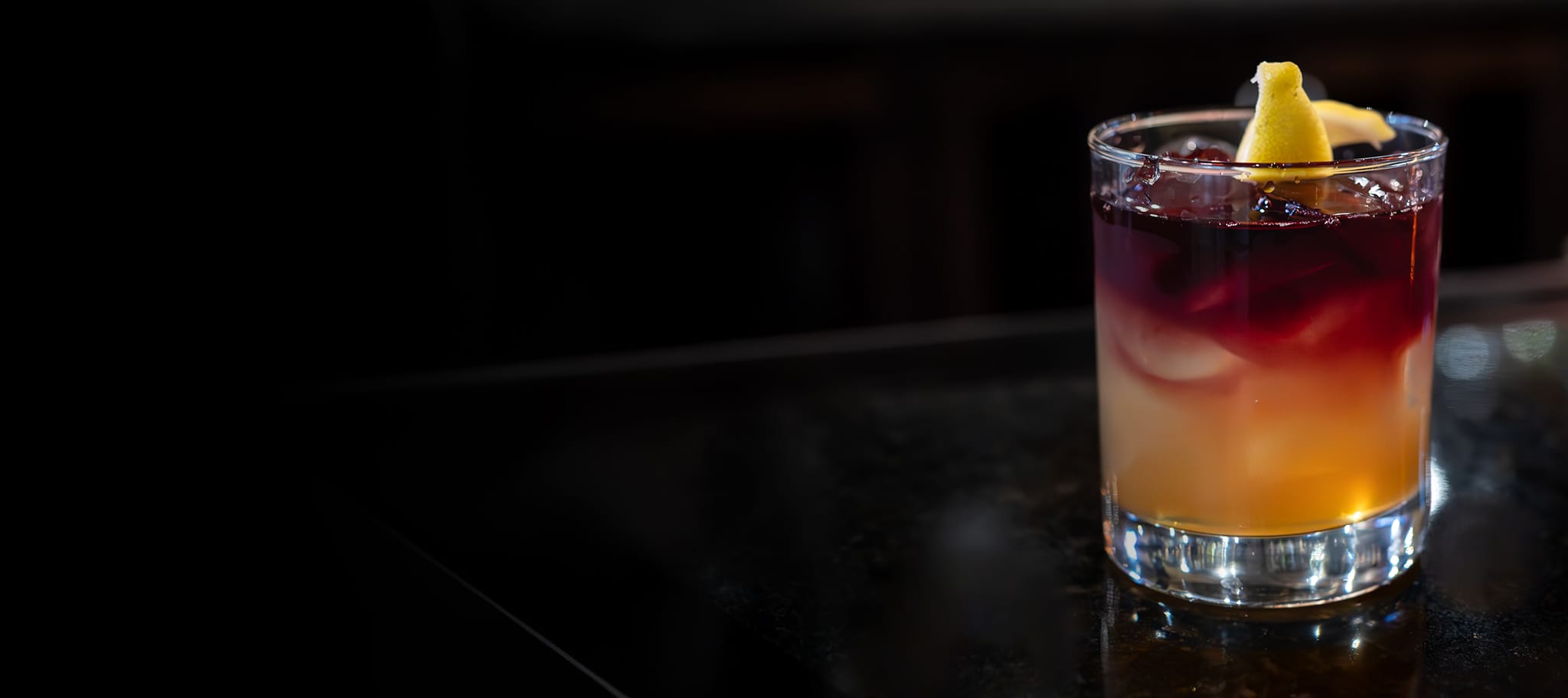 A New York Sour cocktail, with a red wine float on top and lemon twist, sitting on a table