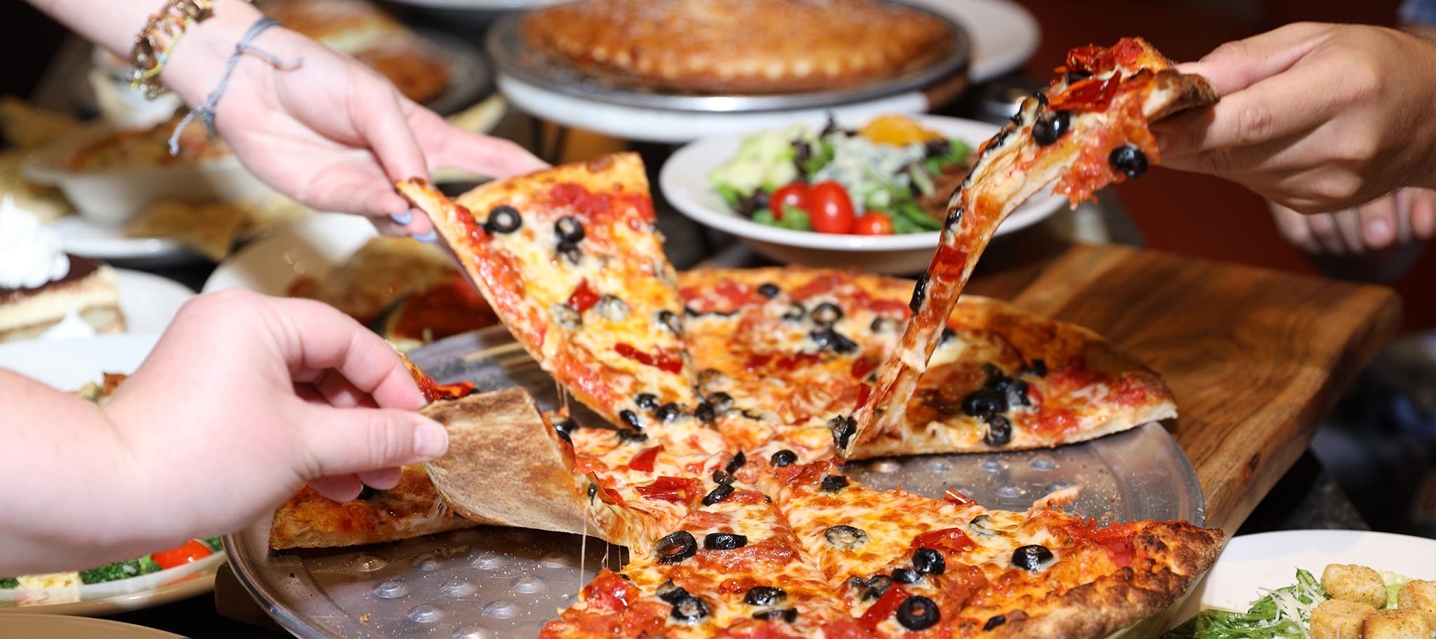 A group of people pulling slices of pizza from a table