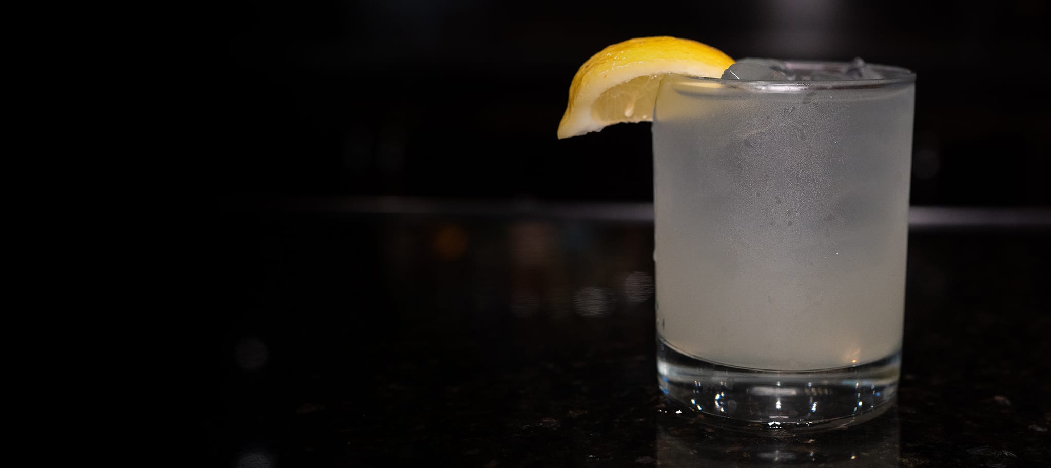 A Cucumber Lemonade Cocktail, with a lemon garnish on the rim of the glass, sitting on a table