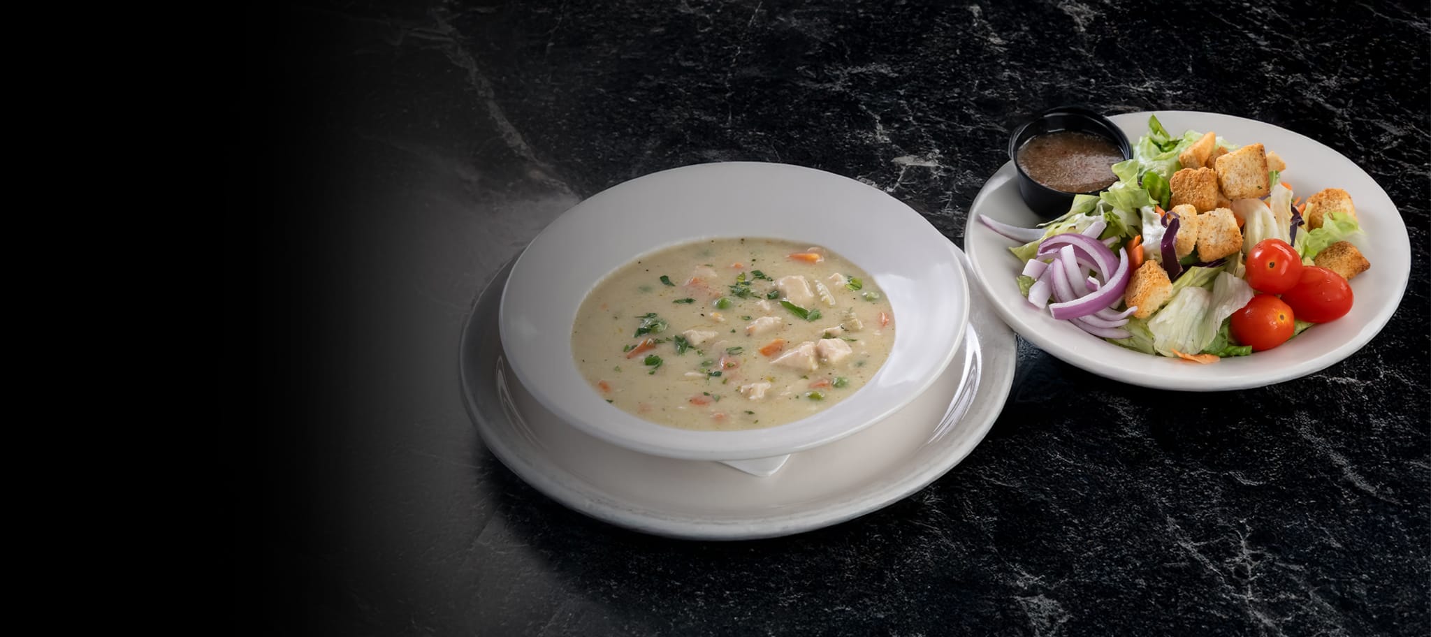 Bowl of soup in white bowl and house salad sitting on a dark tabletop